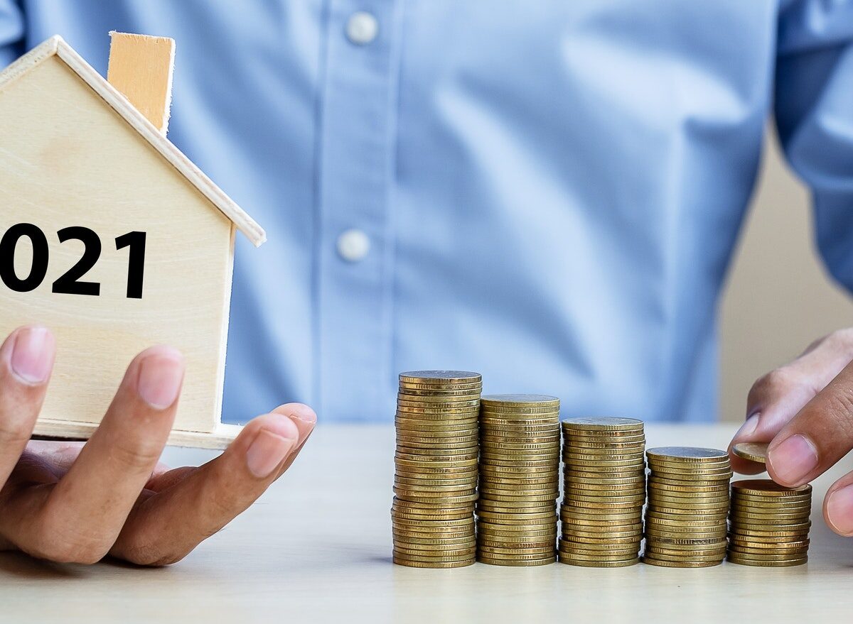 Person holding a house model and coins.